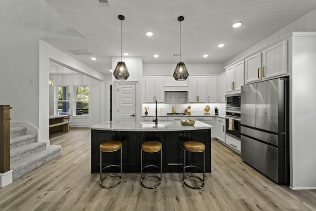 kitchen with decorative light fixtures, stainless steel appliances, white cabinetry, and an island with sink