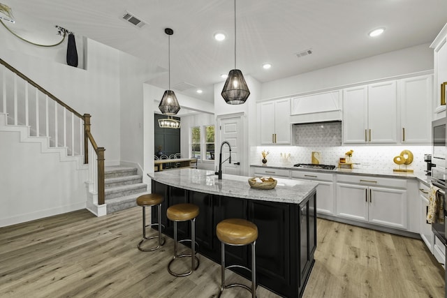 kitchen featuring sink, light stone counters, an island with sink, decorative light fixtures, and white cabinets