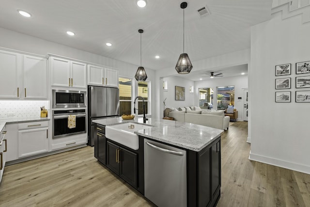 kitchen with stainless steel appliances, ceiling fan, decorative light fixtures, white cabinetry, and an island with sink