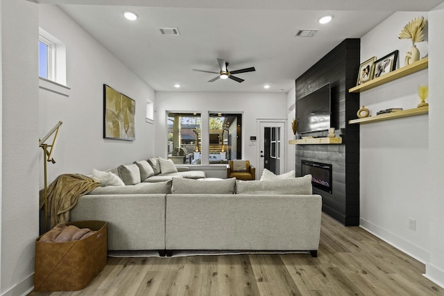 living room featuring a large fireplace, light hardwood / wood-style flooring, ceiling fan, and a healthy amount of sunlight