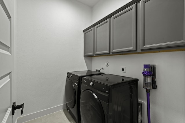 clothes washing area with washer and dryer, cabinets, and light tile patterned floors