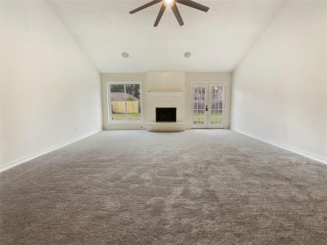 unfurnished living room with ceiling fan, a large fireplace, french doors, a textured ceiling, and carpet