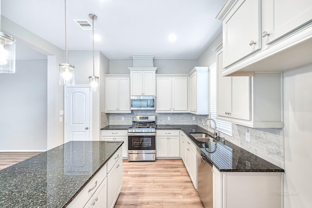 kitchen featuring appliances with stainless steel finishes, sink, dark stone countertops, white cabinetry, and hanging light fixtures