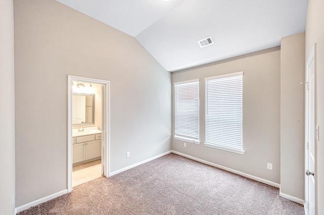 unfurnished bedroom with connected bathroom, multiple windows, carpet, and lofted ceiling