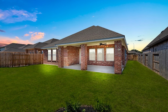 back house at dusk with a lawn, ceiling fan, and a patio area