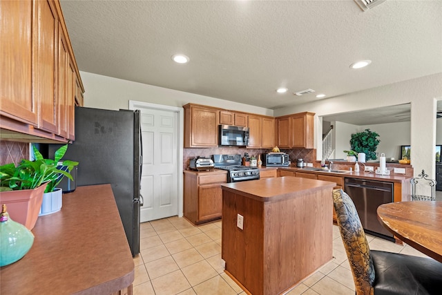 kitchen featuring decorative backsplash, appliances with stainless steel finishes, sink, light tile patterned floors, and a center island