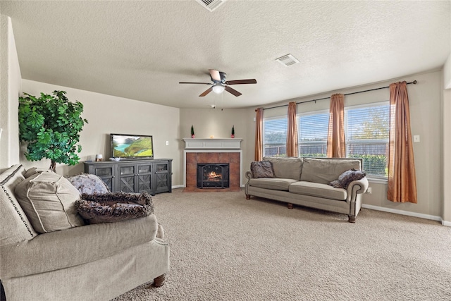 living room with a tile fireplace, a textured ceiling, carpet floors, and ceiling fan