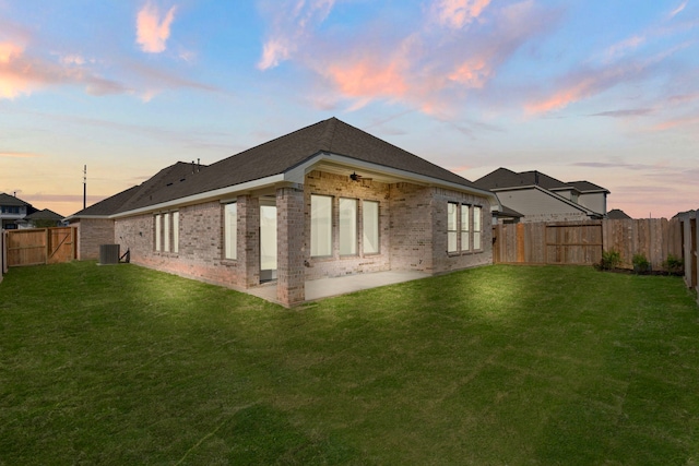 back house at dusk featuring a yard, a patio, and central air condition unit