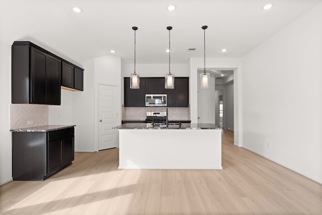 kitchen featuring backsplash, light hardwood / wood-style floors, stainless steel appliances, and an island with sink