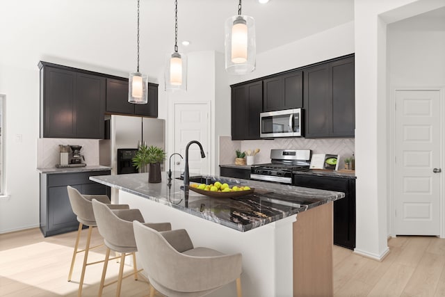 kitchen with a kitchen island with sink, sink, decorative backsplash, appliances with stainless steel finishes, and decorative light fixtures