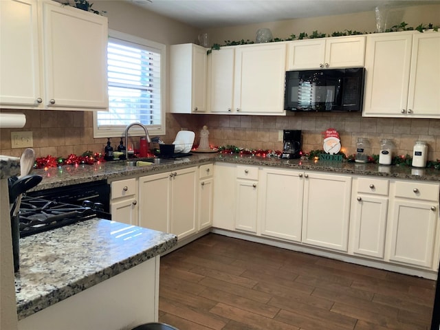 kitchen with sink, dark hardwood / wood-style floors, dark stone countertops, white cabinets, and black appliances