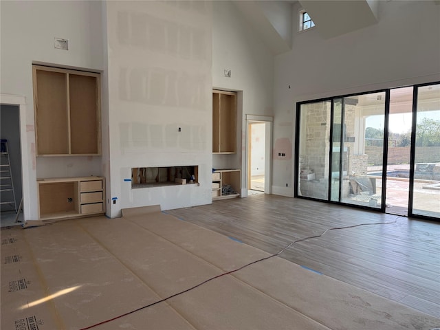 unfurnished living room featuring plenty of natural light, wood-type flooring, a fireplace, and a high ceiling