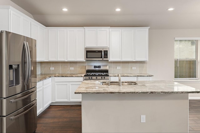 kitchen with a kitchen island with sink, white cabinets, sink, light stone counters, and stainless steel appliances