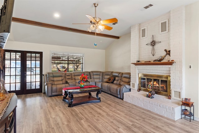 living room with ceiling fan, french doors, a brick fireplace, vaulted ceiling with beams, and light hardwood / wood-style flooring