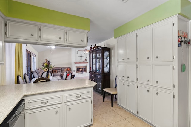 kitchen featuring kitchen peninsula, a brick fireplace, stainless steel dishwasher, white cabinetry, and light tile patterned flooring