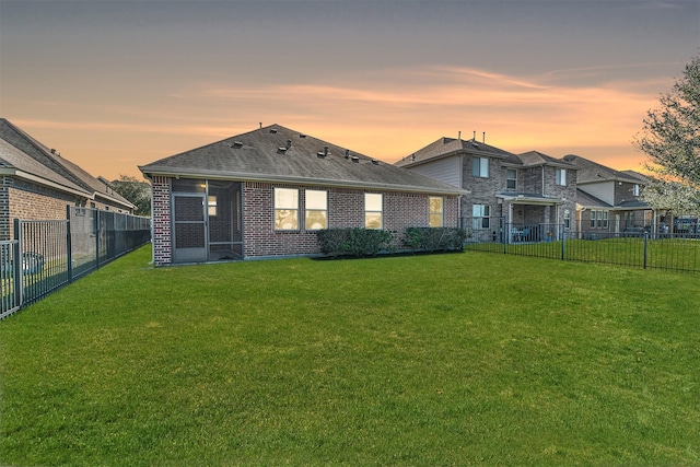 back house at dusk featuring a sunroom and a lawn