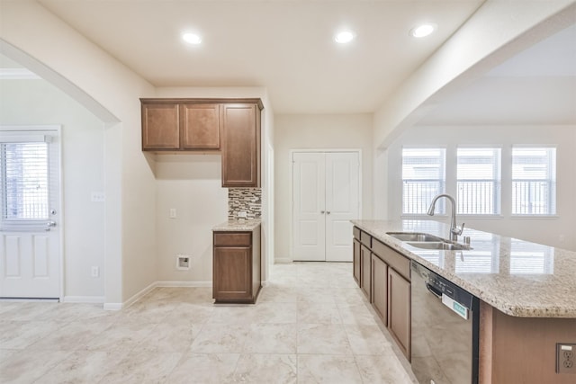 kitchen with dishwasher, a kitchen island with sink, sink, decorative backsplash, and light stone counters