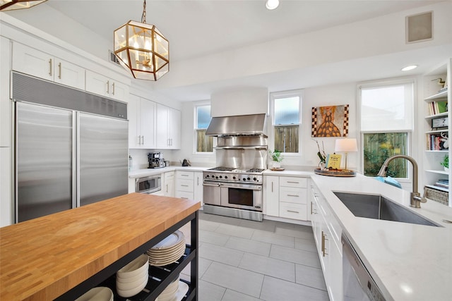 kitchen with sink, wooden counters, built in appliances, pendant lighting, and white cabinets