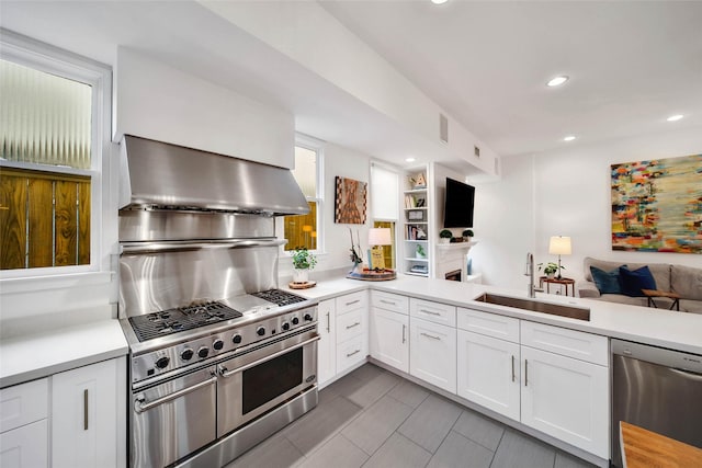 kitchen with white cabinets, sink, wall chimney exhaust hood, appliances with stainless steel finishes, and kitchen peninsula