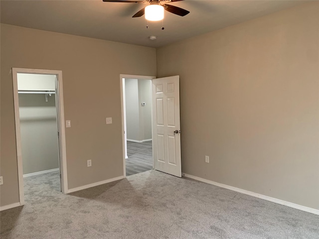 unfurnished bedroom featuring a walk in closet, ceiling fan, a closet, and light colored carpet