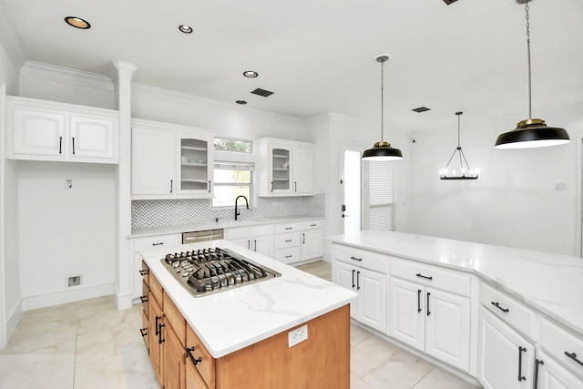 kitchen with white cabinetry, hanging light fixtures, a kitchen island, and light stone counters