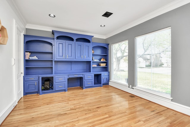 unfurnished office with a healthy amount of sunlight, ornamental molding, built in desk, and light wood-type flooring