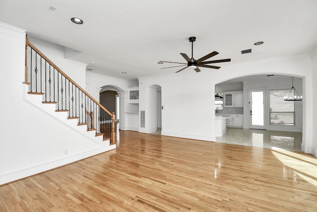 unfurnished living room with ceiling fan with notable chandelier and light hardwood / wood-style floors