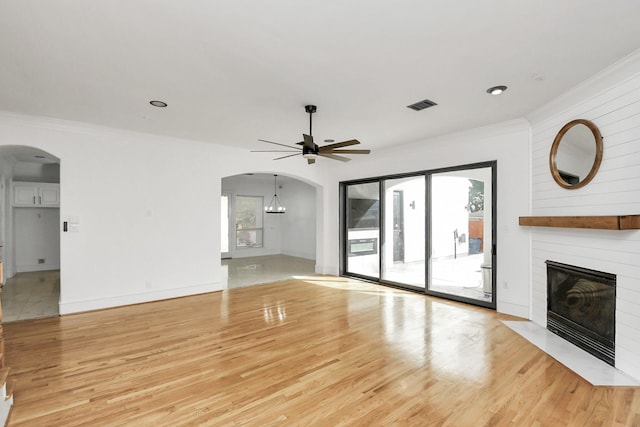 unfurnished living room featuring ceiling fan, ornamental molding, a fireplace, and light hardwood / wood-style flooring