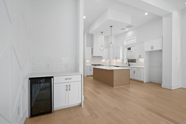 kitchen featuring decorative light fixtures, light hardwood / wood-style flooring, white cabinets, a center island, and wine cooler