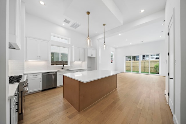 kitchen with white cabinetry, stainless steel dishwasher, a kitchen island, and light hardwood / wood-style floors