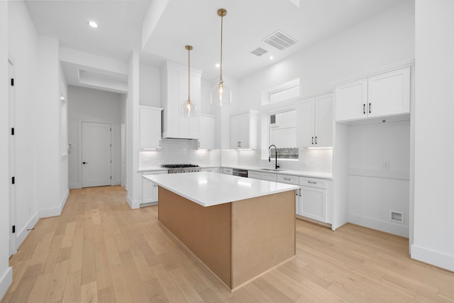 kitchen with white cabinets, sink, hanging light fixtures, light hardwood / wood-style floors, and a kitchen island