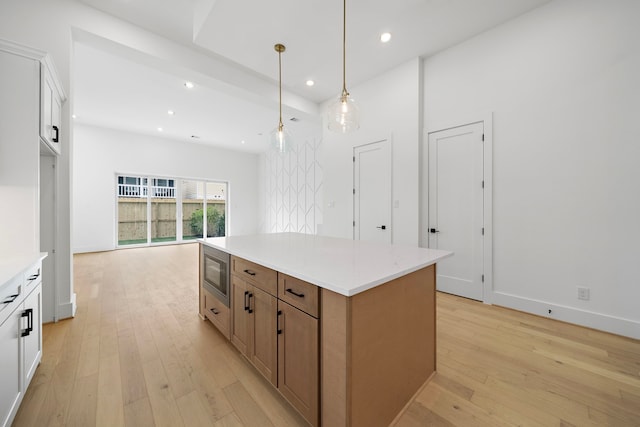 kitchen with decorative light fixtures, white cabinetry, stainless steel microwave, and light hardwood / wood-style flooring