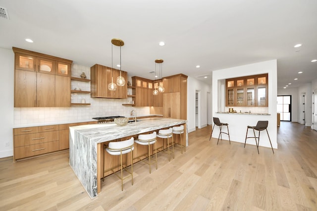 kitchen featuring decorative light fixtures, light hardwood / wood-style floors, a kitchen bar, and tasteful backsplash