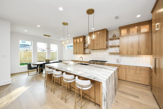 kitchen with pendant lighting, a kitchen island with sink, a kitchen breakfast bar, sink, and light wood-type flooring