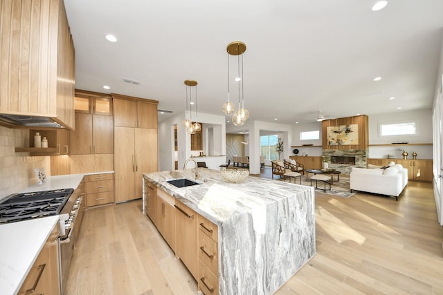 kitchen featuring light stone countertops, a large island, sink, light hardwood / wood-style flooring, and pendant lighting