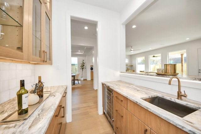 kitchen with sink, beverage cooler, light stone counters, backsplash, and light wood-type flooring