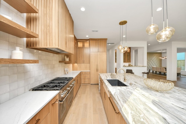 kitchen featuring backsplash, light stone counters, sink, decorative light fixtures, and stainless steel stove