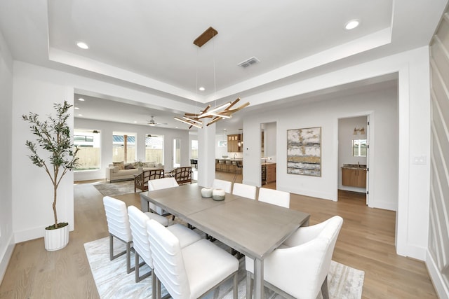 dining area with light wood-type flooring, a raised ceiling, and ceiling fan