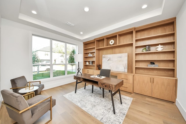 home office with a tray ceiling, built in shelves, and light wood-type flooring