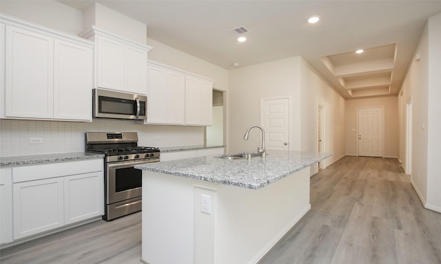 kitchen with a kitchen island with sink, white cabinets, sink, light stone counters, and stainless steel appliances