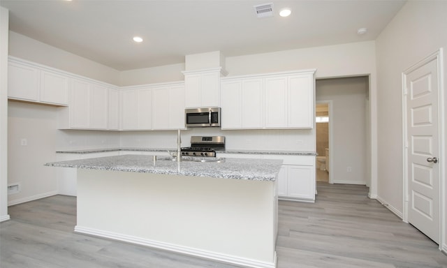 kitchen with a kitchen island with sink, white cabinets, stainless steel appliances, and light stone counters