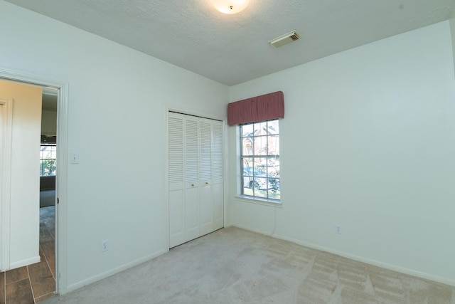 unfurnished bedroom with light colored carpet, a textured ceiling, and a closet