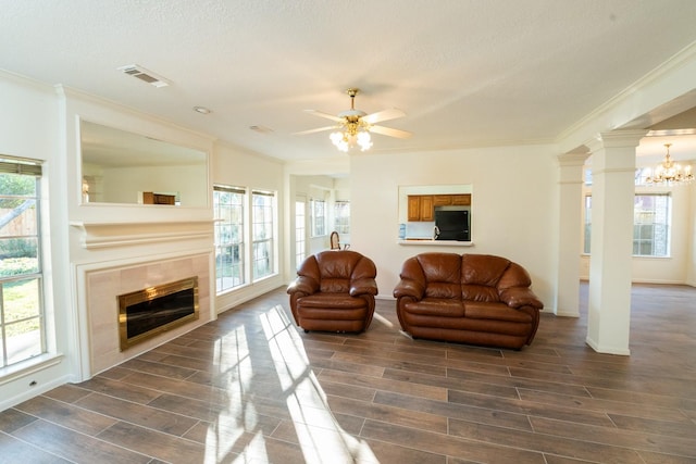 living room featuring ornate columns, a fireplace, ceiling fan with notable chandelier, and ornamental molding