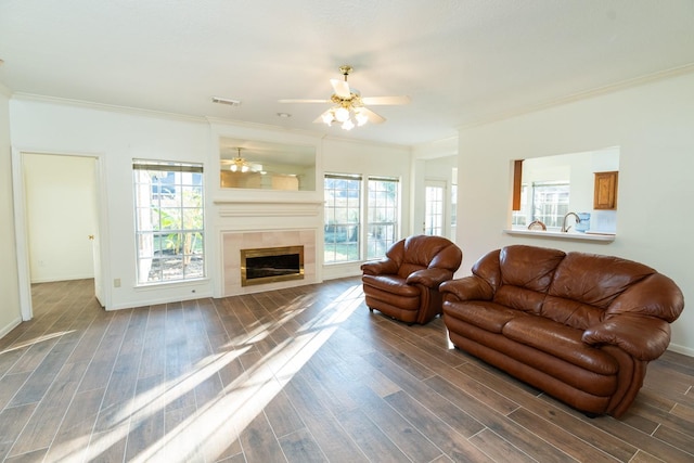 living room featuring a tiled fireplace, a wealth of natural light, crown molding, and dark hardwood / wood-style floors