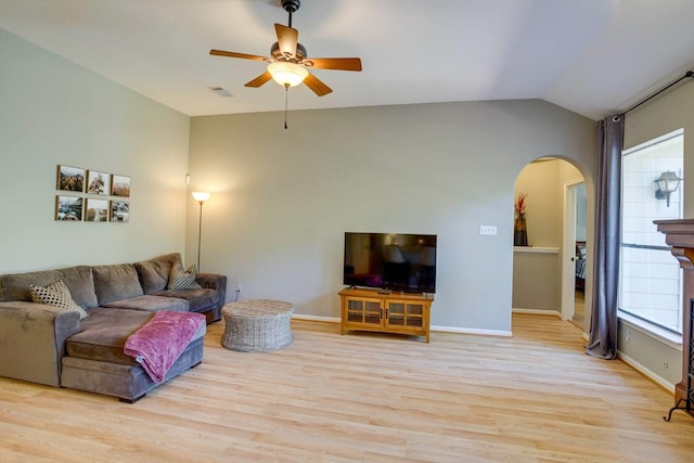 living room featuring ceiling fan, a fireplace, vaulted ceiling, and light wood-type flooring