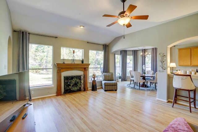 living room with lofted ceiling, light wood-type flooring, ceiling fan with notable chandelier, and a wealth of natural light