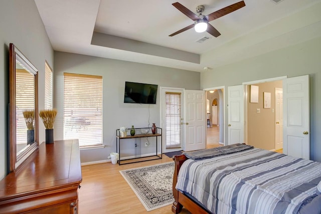 bedroom featuring light wood-type flooring, a raised ceiling, and ceiling fan