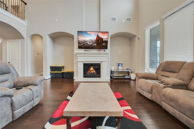 living room featuring a towering ceiling and dark wood-type flooring