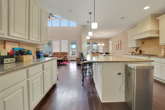 kitchen with light stone countertops, dark hardwood / wood-style flooring, an island with sink, decorative light fixtures, and custom exhaust hood