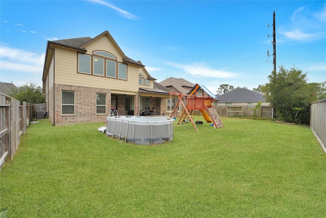 rear view of property with a fenced in pool, a playground, and a yard